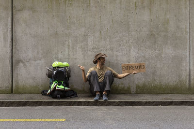 Man holding cardboard with entire world text while sitting against wall 