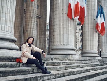 Portrait of smiling mid adult woman sitting on steps by historic building