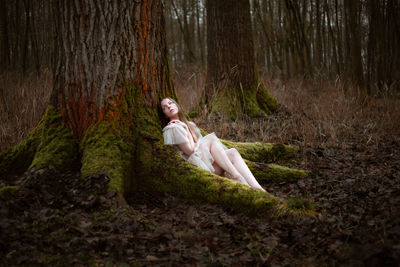 Side view of woman sitting in forest covered with moss