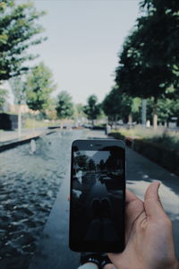 Man photographing smart phone against sky