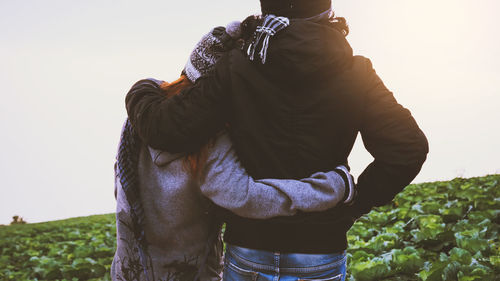 Rear view of couple standing on field against clear sky