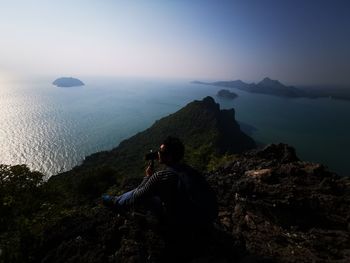 Man sitting on rock against sky