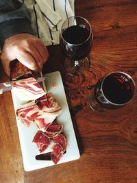 Cropped image of man cutting meat with red wine served on table