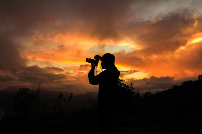 Silhouette man photographing against sky during sunset