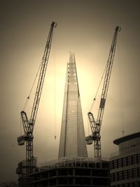 Low angle view of cranes with shard london bridge against clear sky