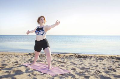 Woman practicing yoga pose at beach against clear sky