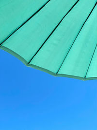 Low angle view of turquoise sun umbrella against clear blue sky