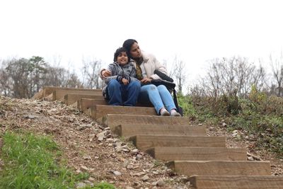 Low angle view of mother with daughter sitting on steps against clear sky