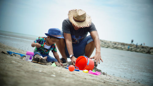 Father and son playing with toys at beach against sky