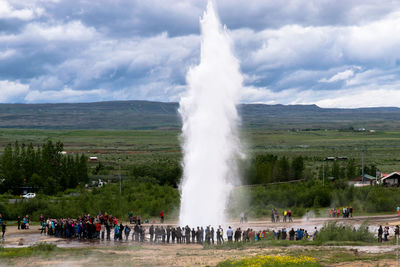 People looking at strokkur geyser against cloudy sky