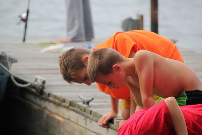 Side view of male friends looking down while kneeling on pier
