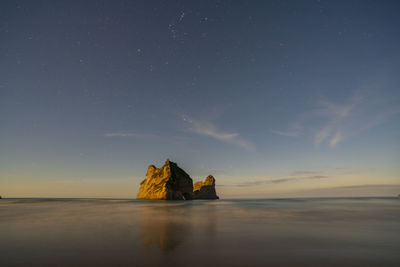 Scenic view of rocks at sea against sky at sunset