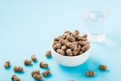 Rye bran in a bowl and on the table and a glass of water on a blue background