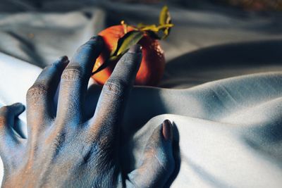 Cropped messy hand of woman with orange on bed sheet