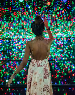 Rear view of woman standing against illuminated lights at night