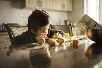 Little boy in kitchen at the table peeling vegetables, helping his mother. mother's day, women's day