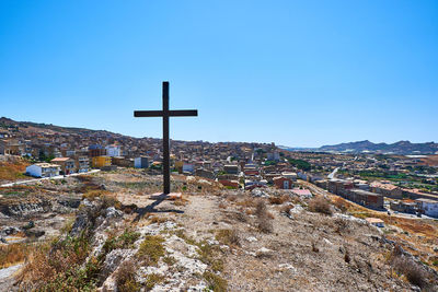 Cross amidst buildings against clear blue sky