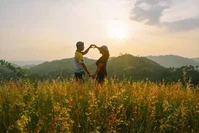 Couple making heart shape with hands against mountains during sunset