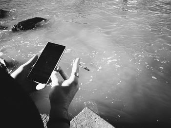 Cropped hand of person using mobile phone over lake