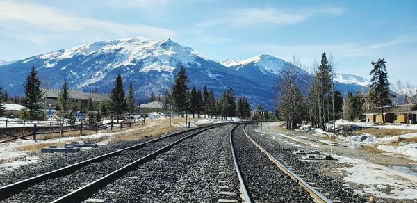 Railroad tracks by snowcapped mountains against sky