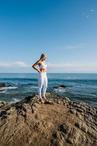 Female athlete standing on rocky beach, looking towards the sun