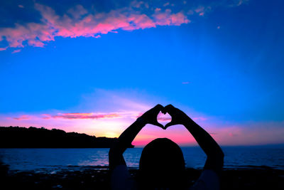 Rear view of silhouette woman making heart shape against sky during sunset