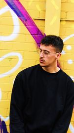 Portrait of young man standing against graffiti wall