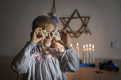 Cute girl holding star shape while standing against burning candles