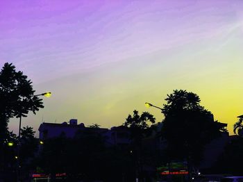 Low angle view of silhouette trees and buildings against sky at sunset