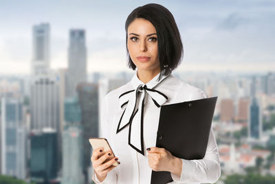 Portrait of young woman using mobile phone in city