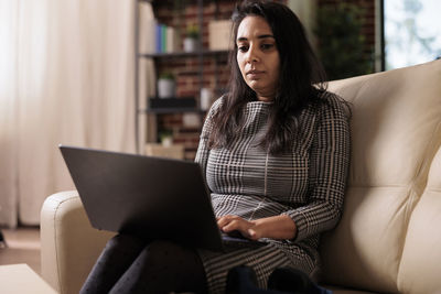 Young woman using laptop while sitting on sofa at home