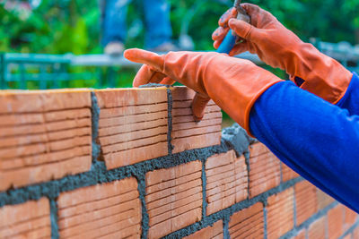 Construction worker laying down brick wall using mortar to join and fill in the gap between bricks