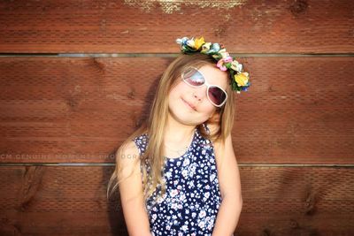 Portrait of cute girl wearing sunglasses and wreath against wooden wall