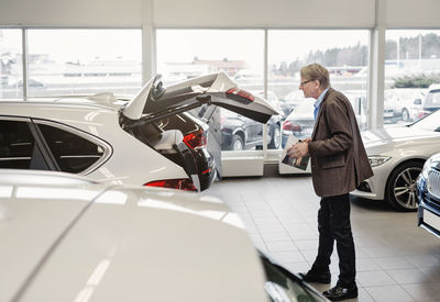 Side view of senior man examining car trunk at showroom