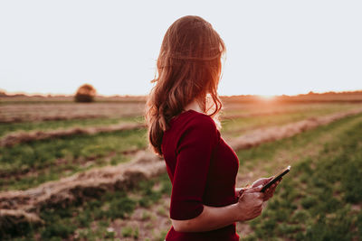 Side view of woman using mobile phone while standing on land against clear sky