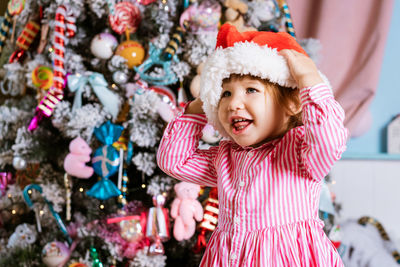 Happy little girl wearing pink dress and wearing santa hat looking to side