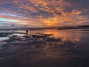 Scenic view of beach against cloudy sky during sunset