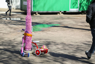 Cropped image of man walking by bicycle and push scooter tied up with crocheted pole on footpath