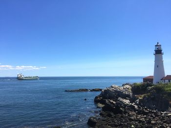 Lighthouse by sea against clear blue sky