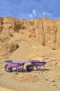 Empty chairs and rocks on sand against sky