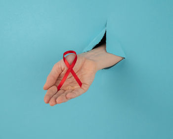 Cropped hand holding tape measure against blue background