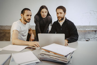 Male and female professionals working over laptop on table in startup company