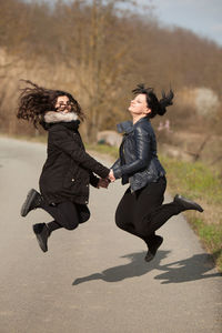 Side view of happy female friends jumping on road