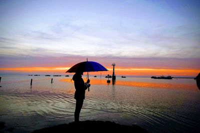 Silhouette people on beach against sky during sunset