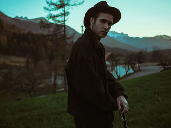 Portrait of young man holding guitar while standing on field during sunset