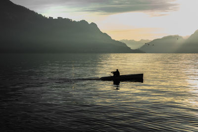 Silhouette man sitting on boat in lake against sky during sunset