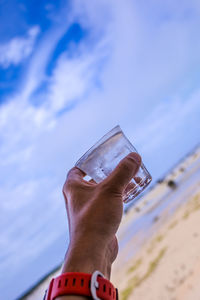 Midsection of man holding glass against sky
