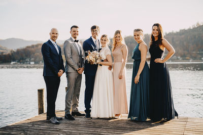 Bride and groom standing along with friends on jetty over lake