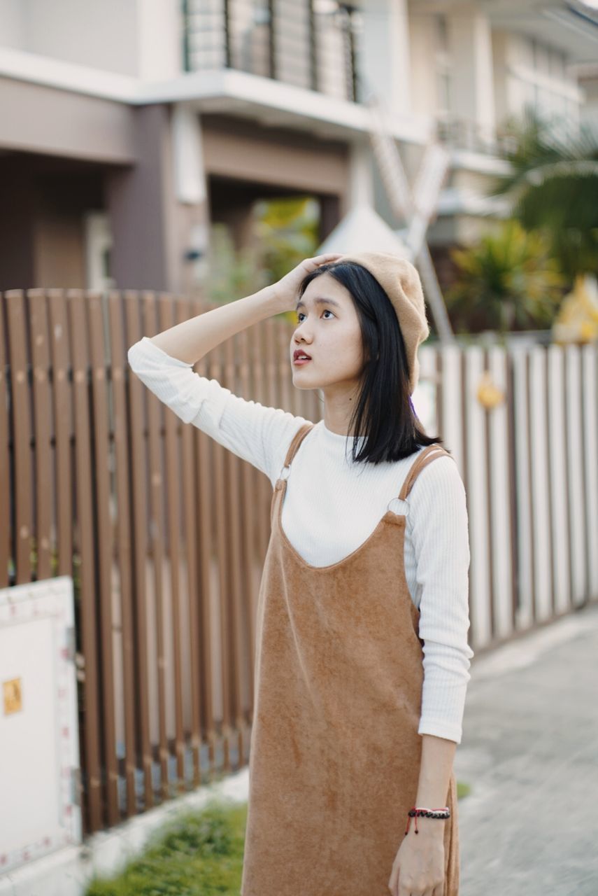 standing, one person, architecture, real people, casual clothing, focus on foreground, lifestyles, young women, building exterior, looking, built structure, day, leisure activity, looking away, women, three quarter length, young adult, hair, hairstyle, human arm, outdoors, arms raised, beautiful woman
