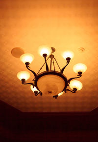 Low angle view of illuminated light bulb hanging against ceiling